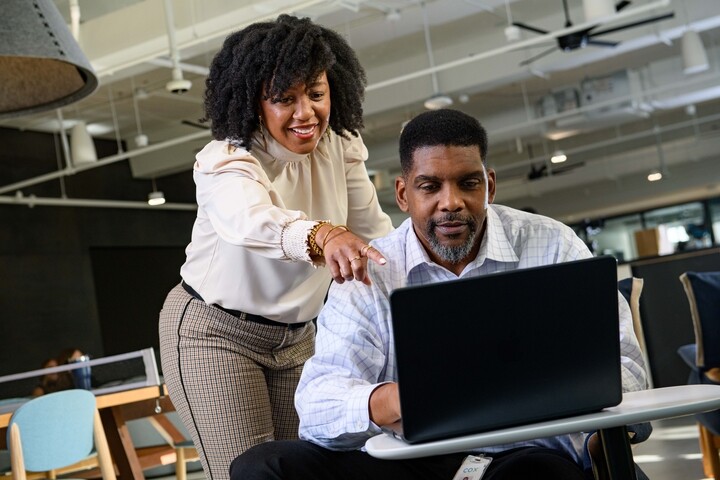 a person pointing at a person using a laptop