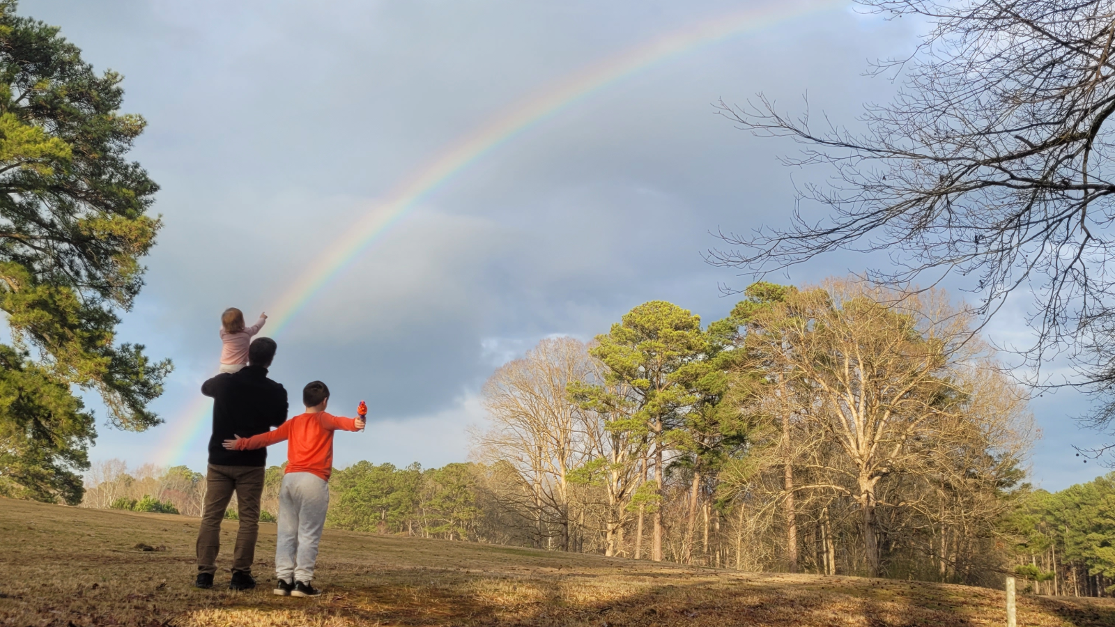 a group of people standing in a field with a rainbow