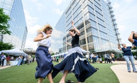 Cox employees dancing in a grassy area with a large building in the background