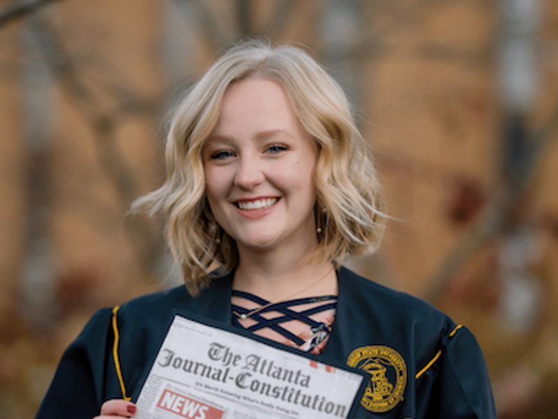 An AJC employee holding up her graduation cap