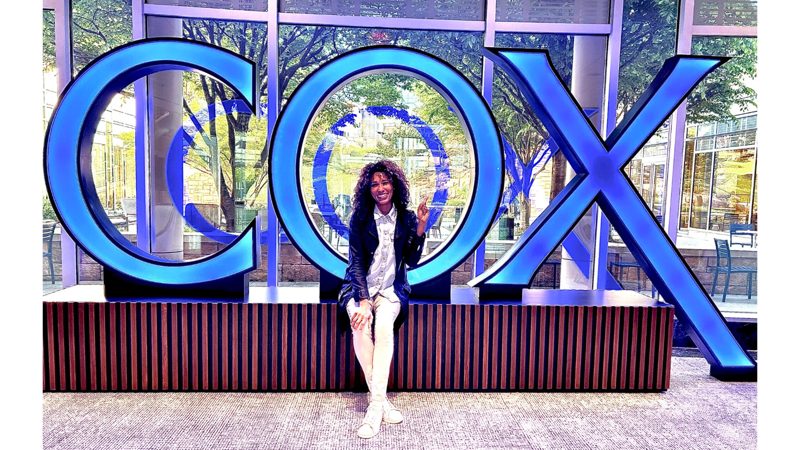 a Cox employee sitting on a bench in front of a large sign
