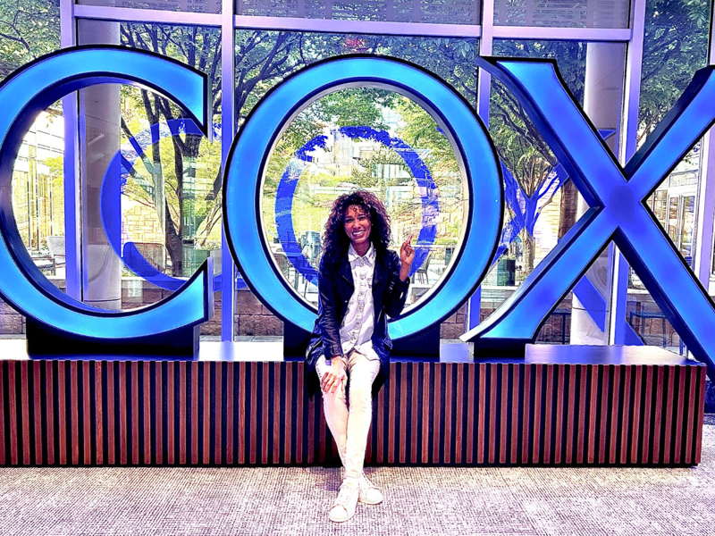 a Cox employee sitting on a bench in front of a large sign