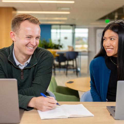 a person and person sitting at a table with laptops and a book