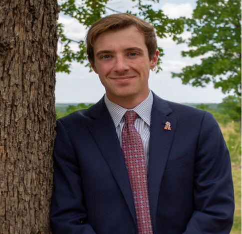 a person in a suit leaning against a tree