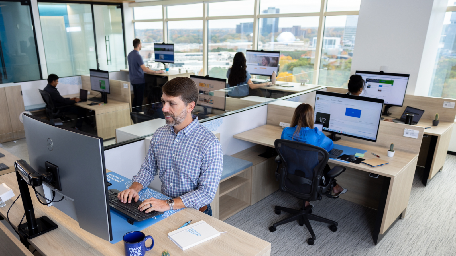 a person sitting at a desk in an office with people working on computers
