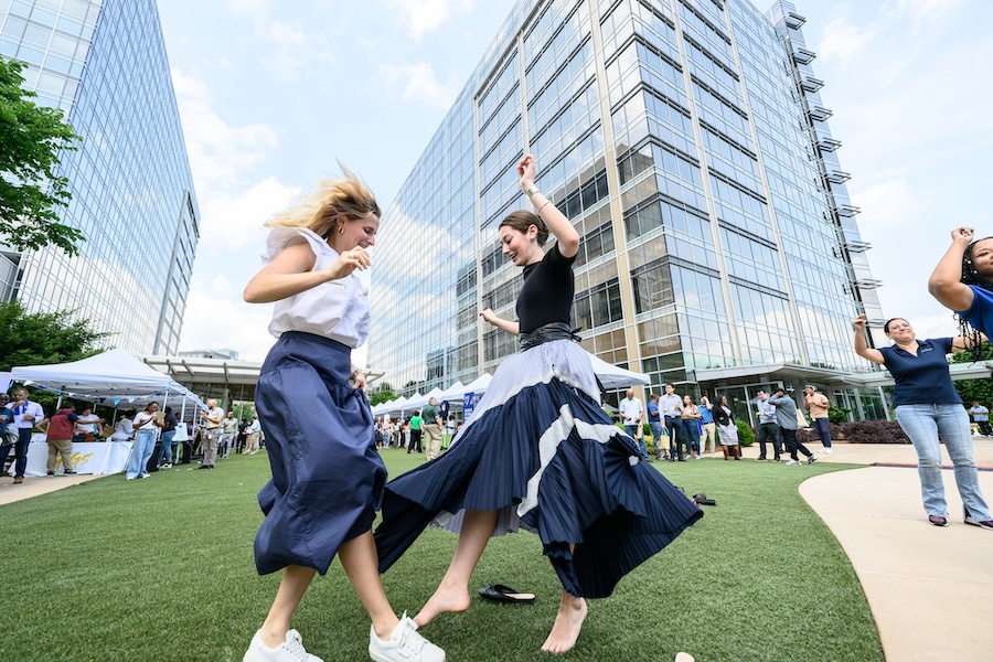 two women dancing in a grassy area with a large building in the background