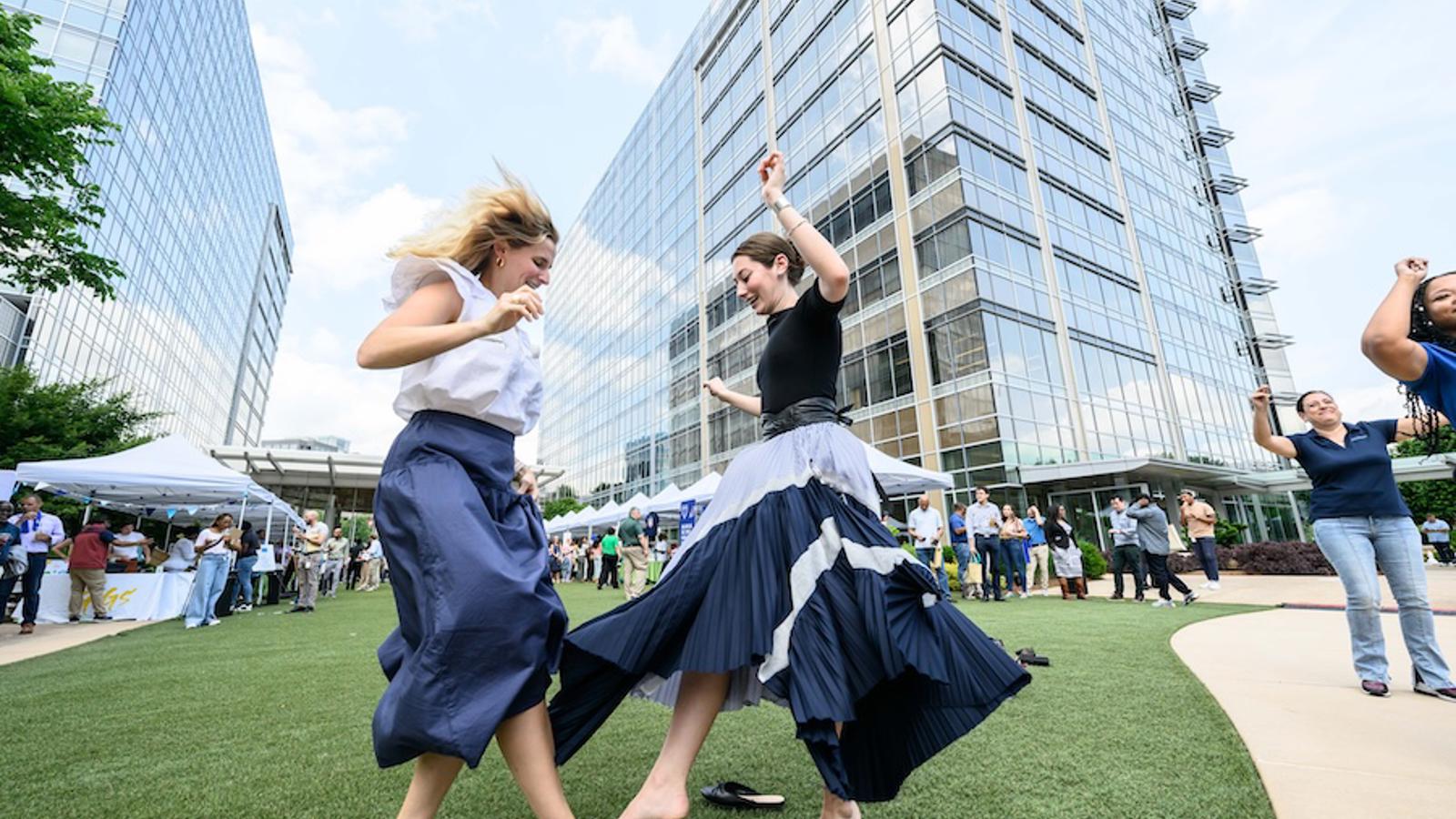 two women dancing in a grassy area with a large building in the background