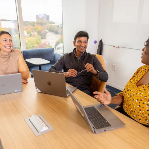 a group of people sitting around a table with laptops