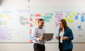 a person and person standing in front of a whiteboard with post-it notes
