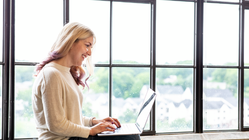 Cox employee working on laptop in front of window