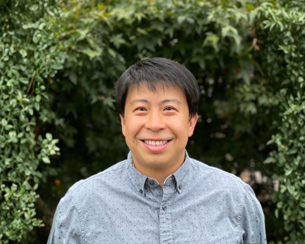 a person smiling in front of bushes